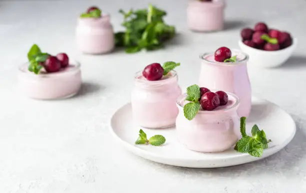 Photo of Delicious Italian dessert cherry panna cotta with fresh cherries and mint in jars. Light grey stone background, selective focus. Copy space.