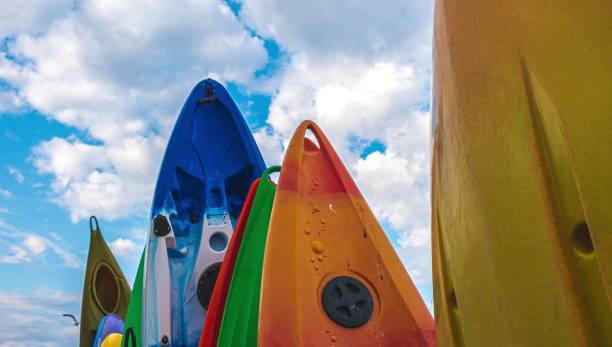 Group of various sized paddle boards standing up in their rack against a blue sky background with clouds