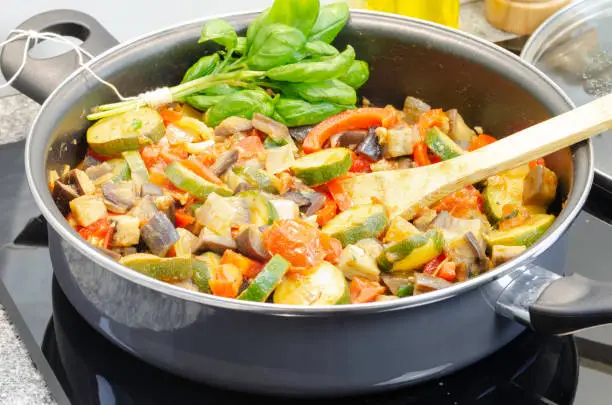 Mediterranean-style vegetable stew called traditional french ratatouille with freshly mixed vegetable in a cooking pan on a black induction heater
