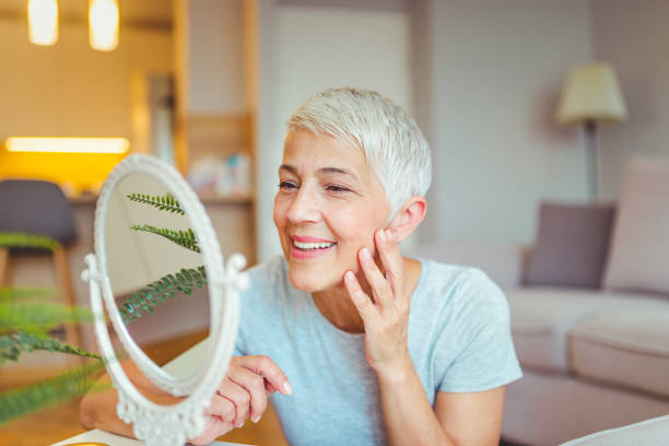 Good skincare habits will have you looking younger Happy mature woman admiring herself in the mirror. Middle aged woman looking at wrinkles in mirror. Plastic surgery and collagen injections. Makeup. Good skincare habits will have you looking younger innocence stock pictures, royalty-free photos & images