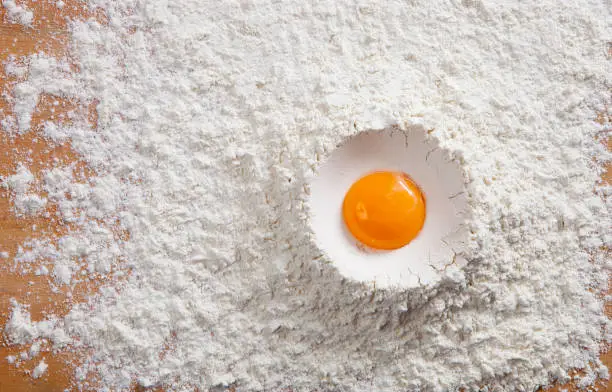 Photo of Fresh raw egg yolk in pile of white flour with copy space. Top view, horizontal close-up.