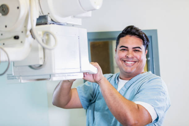 Technologist using x-ray machine A mid adult Hispanic man working in a medical imaging center as a technologies, using an x-ray machine. He is smiling at the camera. x ray equipment stock pictures, royalty-free photos & images