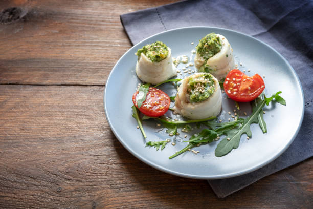 istock Fish fillet rolls from plaice filled with mashed celery and arugula, grilled tomatoes, rocket salad and sesame seed on a blue plate on a rustic wooden table, spring time appetizer for Easter holidays, copy space 1208675756