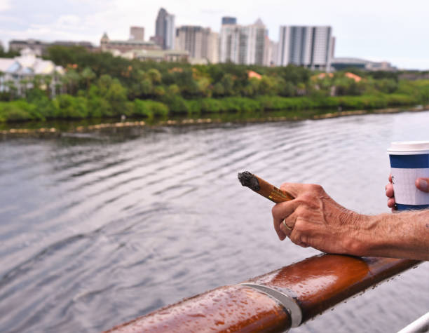 Detail of the hand of a smoking man holding a burning cigar Detail of the hand of a smoking man holding a burning cigar in a cruise ship depicting success, wealth and relaxation. cuban man smoking big cigar stock pictures, royalty-free photos & images