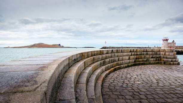 Curved stone steps in front of Howth Lighthouse with Irelands Eye island in background. Cloudy weather in Howth harbour, Dublin, Ireland