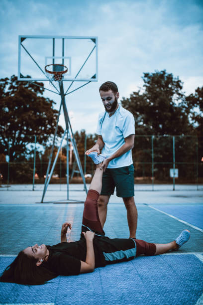 atleta maschile che aiuta donna ferita sul campo da basket - athlete coach basketball male foto e immagini stock