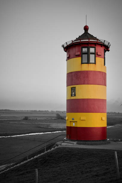 Pilsum Lighthouse on a dyke on the North Sea coast. The yellow and red striped \
