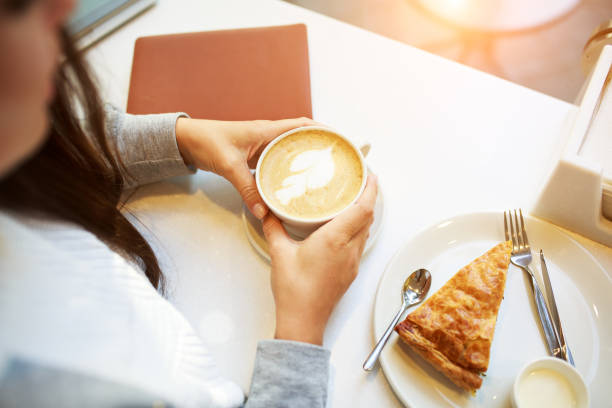 istock Young smiling woman doing a coffe break sitting in cafe, with notebook and cup of coffe or latte , spinach pie, overhead view 1208684676