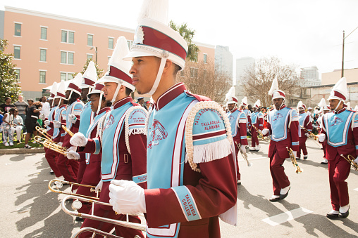 In New Orleans, United States a college marching band walks in formation along the street in a Mardi Gras parade during the day.