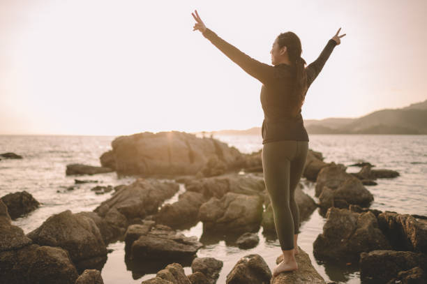 une fille chinoise asiatique d’adolescent regardant la mer avec le signe de main souriant pendant le coucher du soleil - success determination idyllic carefree photos et images de collection