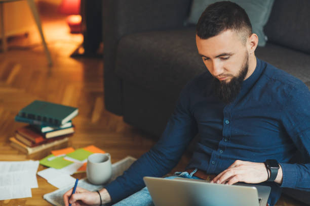 istock Handsome caucasian entrepreneur with big beard is working at his laptop while writing something and drinking a coffee 1208698311