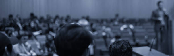 istock Conference photo audience and speaker giving speech. Seminar presenter on a panel during forum. Corporate manager in sales executive training discussion on stage. Investor pitch presentation. 1208702269