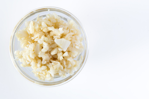 Crushed Garlic in glass bowl. Healthy Food Concept Top View on white background