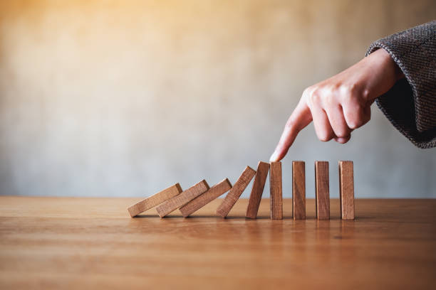 istock a finger try to stop falling wooden dominoes blocks for business solution concept 1208710323