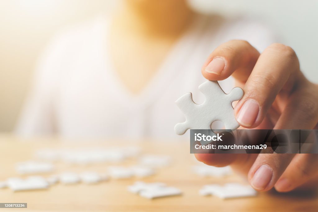 Hand of male trying to connect pieces of white jigsaw puzzle on wooden table. Healthcare for Alzheimer disease, dementia, memory loss, autism awareness and mental health concept Mental Health Professional Stock Photo