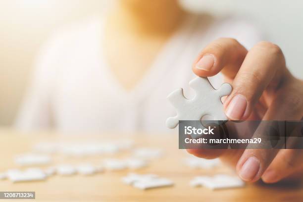 Hand Of Male Trying To Connect Pieces Of White Jigsaw Puzzle On Wooden Table Healthcare For Alzheimer Disease Dementia Memory Loss Autism Awareness And Mental Health Concept Stock Photo - Download Image Now