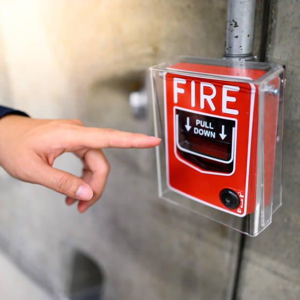 Male hand pointing at red fire alarm switch Male hand pointing at red fire alarm switch on concrete wall in office building. Industrial fire warning system equipment for emergency. emergency break glass box stock pictures, royalty-free photos & images
