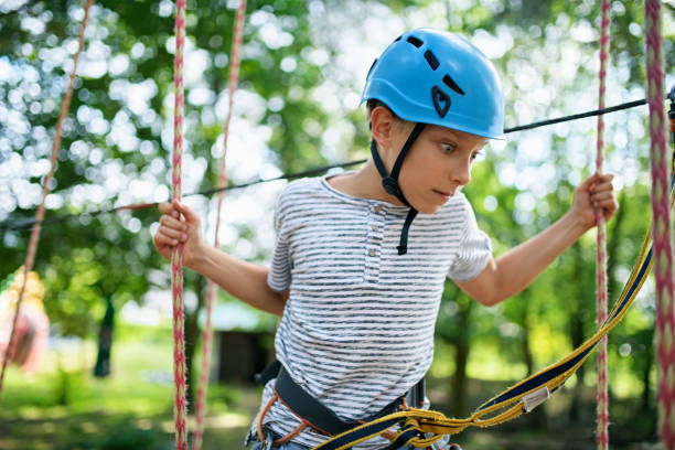 Little boy in ropes course in adventure park. \nSunny summer day. The boy is scared of heights.\nNikon D850