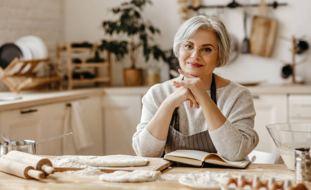 счастливая старуха бабушка повара на кухне месит тесто, печет печенье - grandmother domestic life cooking domestic kitchen стоковые фото и изображения