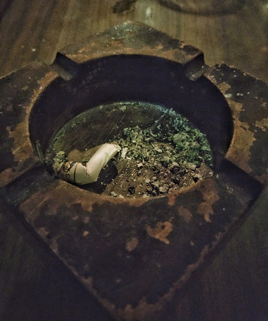 close up image of a stubbed cigarette bud and ash in a wooden ashtray