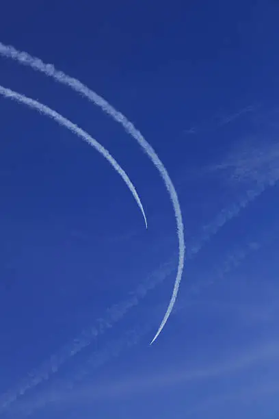 Two cureved traces of jet-fighters against blue sky