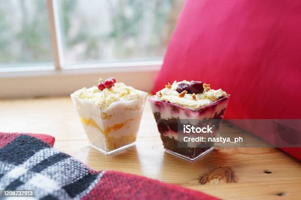 Two Colorful Biscuit Desserts With Berries And Cream In Glasses On Table Near The Window Stock Photo - Download Image Now