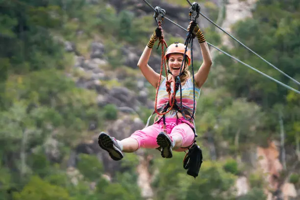Young joyful woman rappelling from a zip line during canopy tour in nature and looking at camera.
