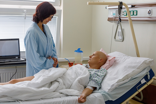 Woman without hair after chemotherapy patient lying at hospital bed feeling sad and depressed worried. A friend came to please her. Health care and clinical attention concept.