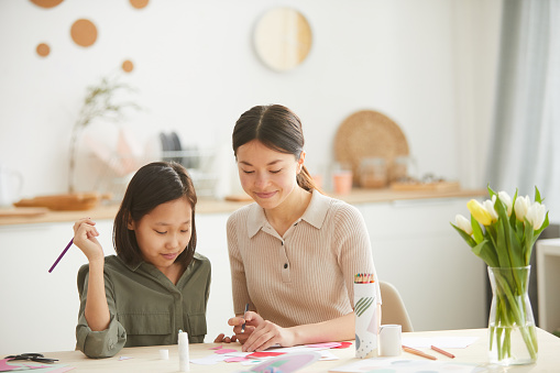 Young Asian woman helping her teen sister to create handmade Mothers Day holiday card, horizontal shot, copy space