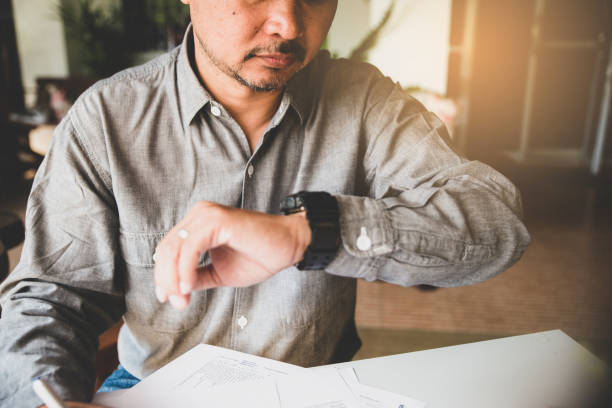 hombre de negocios profesional que ve el reloj de pulsera para comprobar la hora en la oficina - deadline urgency calendar women fotografías e imágenes de stock