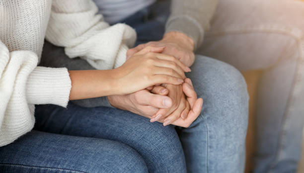 istock Unrecognizable Couple Holding Hands Sitting On Couch Indoor, Cropped 1208749684