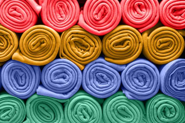 Rolls of colored rugs lie on a shelf, texture effect.