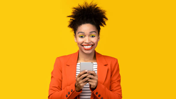 istock Afro girl holding cell phone in yellow studio 1208753831