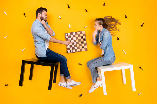 Top view above high angle flat lay flatlay lie view concept of her she his he nice focused clever spouses, sitting on stool playing chess isolated on bright vivid shine vibrant yellow color background