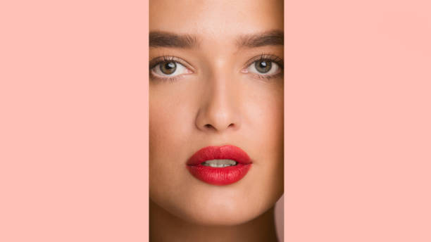 istock Girl with red plump lips looking through pink paper frame 1208754275
