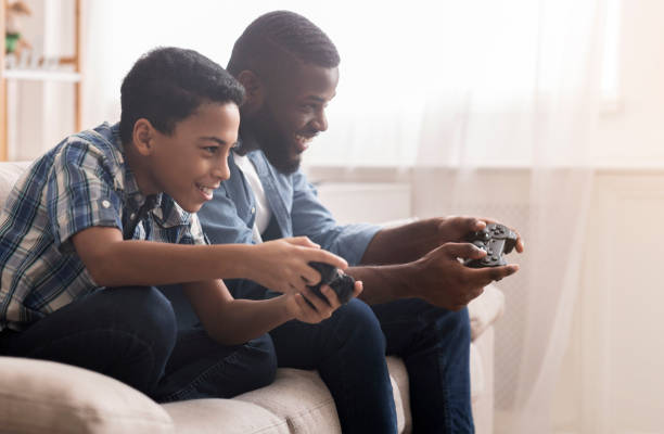 afro ojciec i syn gra w gry wideo z joystickami - handheld video game video game technology playing zdjęcia i obrazy z banku zdjęć