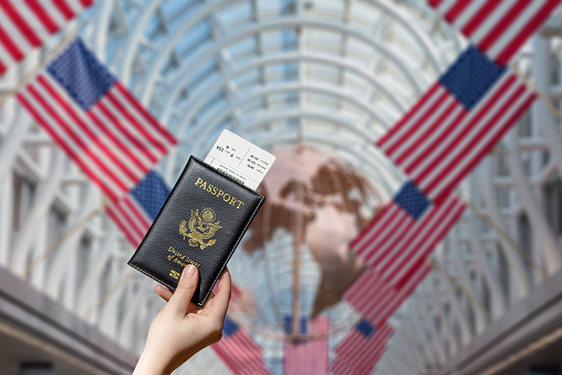 Woman hand holding american passport with boarding pass in the Chocago airport with american flags. concept. America. USA