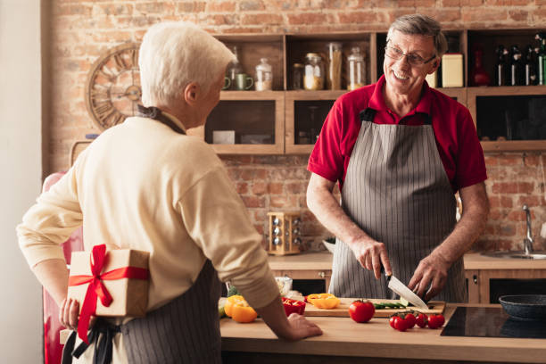 istock Caring elderly woman preparing gift for her happy husband at kitchen 1208759827