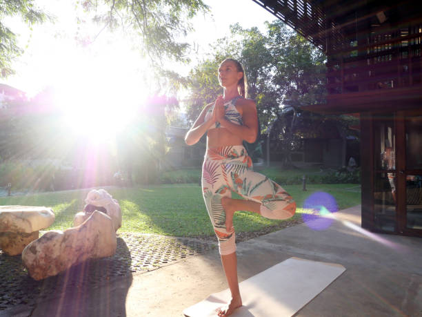 Young woman in tree yoga pose standing in courtyard in sun flare Young woman in tree yoga pose standing in courtyard in sun flare. contributor stock pictures, royalty-free photos & images