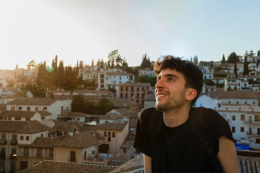 Happy travelling young bearded backpacker smiling with Granada Albaycin cityscape. Wanderlust and living the moment visiting Andalusia Spain, enjoying tourism and sunsets.