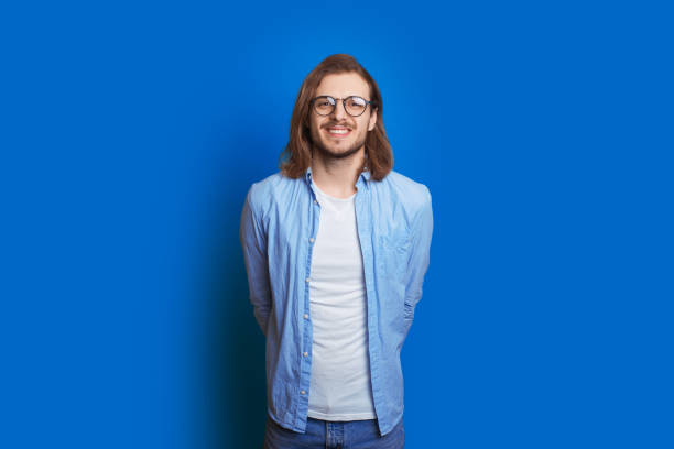 Confident caucasian man with beard and long hair posing on a blue background while hiding his hand behind back