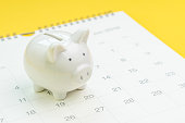 Finance, saving money or salary pay day, white piggy bank on white clean calendar on solid yellow background