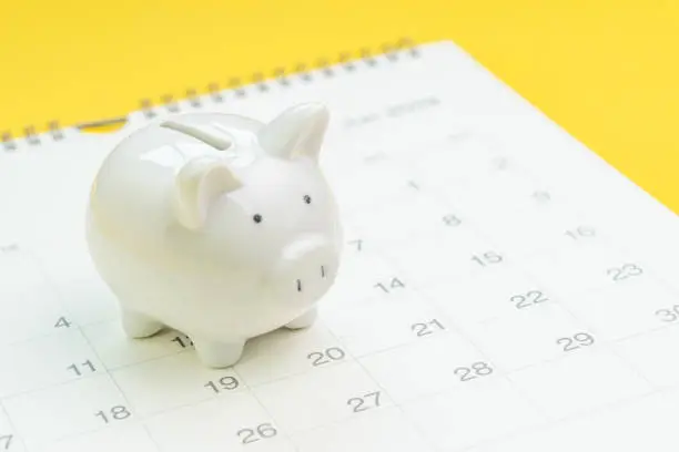 Photo of Finance, saving money or salary pay day, white piggy bank on white clean calendar on solid yellow background