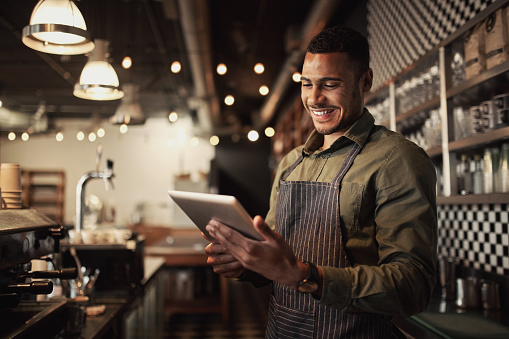 Cheerful black cafe owner behind counter using digital tablet