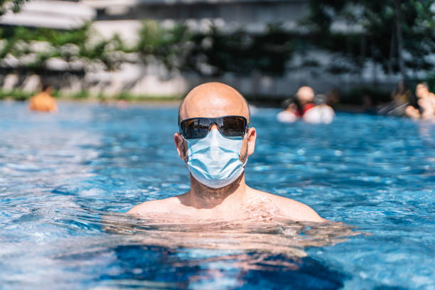 portrait of a tourist couple wearing a protective mask inside the pool for fear of the coronavirus covid19 stock photo