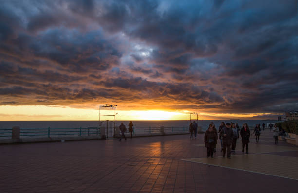 People walking on the Genoa promenade under a cloudy sky at sunset,  Italy stock photo