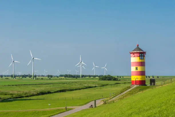 The famous Pilsum Lighthouse with wind turbines in the background near the East Frisian village of Greetsiel on the German North Sea coast of Lower Saxony. The lighthouse was built in 1891 and became famous as one of the central locations of the movie Otto – Der Außerfriesische ("Otto – the Outer Frisian") by the German comedian Otto Waalkes.