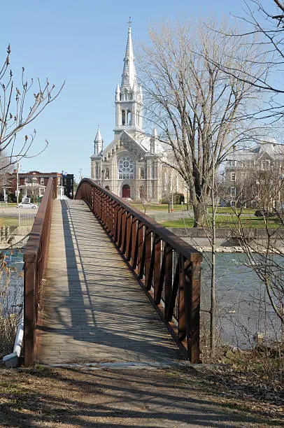 A pedestrian bridge goes to a church in a sunny spring afternoon, at Chateauguay, Quebec, Canada