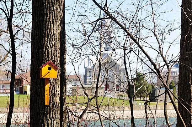 A yellow birdhouse with, in background, a majestic church, in Chateauguay, Quebec, Canada.
