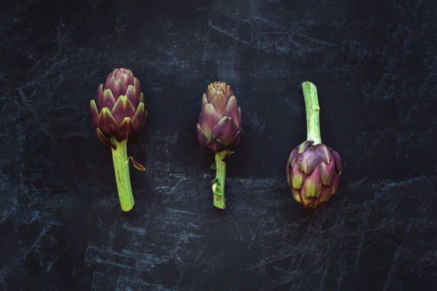 istock Three ripe artichokes on a black chalk board. Top view, flat lay. 1208780883